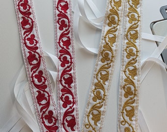 Puede incluir: Dos pares de bandas de tela bordadas con lazos de cinta blanca. Un par presenta diseños florales rojos sobre fondo blanco, el otro bordados florales dorados. Las bandas son probablemente decorativas.