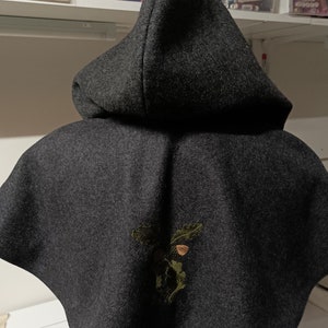 Op de afbeelding: Een donkergrijze capuchonmantel met een groene en bruine eikel geborduurd ontwerp.