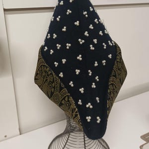 May include: A black felt hat with a pointed crown and a gold and black patterned brim. The hat is decorated with white pearl-like beads.