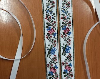 Puede incluir: Dos correas de tela blanca con diseños florales bordados en verde, azul, rosa y rojo.