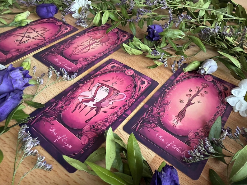 May include: Four rectangular tarot cards with a vibrant magenta and purple color palette, featuring illustrations of a pentacle, a sword, a teacup, and a wand. Each card is labeled with its name, including Ace of Cups and Ace of Wands.