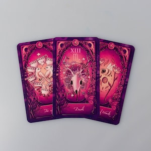 May include: Three tarot cards with a purple and pink background. The cards are "Ten of Cups", "Death", and "Wands".
