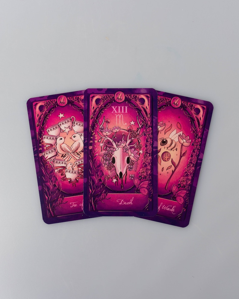 May include: Three tarot cards with a purple and pink background. The cards are "Ten of Cups", "Death", and "Wands".