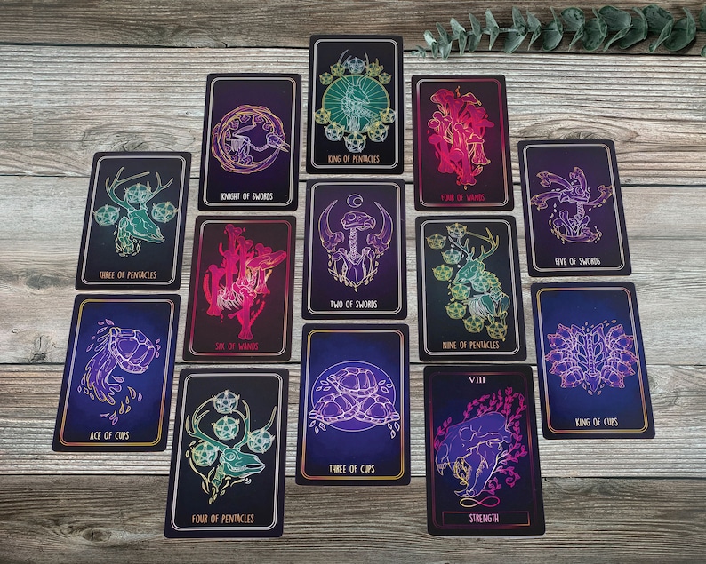 May include: A collection of tarot cards with dark blue and purple backgrounds. Each card features unique illustrations in teal, pink, and gold, with titles such as "Knight of Swords," "Strength," and "King of Pentacles."