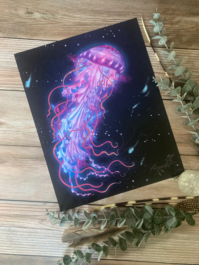 May include: A vibrant art print featuring a jellyfish illustration. The jellyfish is depicted in shades of pink, purple, and blue against a dark background. The tentacles are long and flowing, and the overall design has a dreamy, ethereal quality.