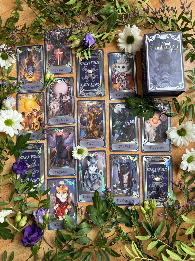 May include: A deck of The Crooked Cat Tarot cards featuring feline illustrations on each card, including The Hanged Man, Justice, The Empress, The Moon, The Star, The Fool, The Lovers, Judgement, The High Priestess, and The Magician.
