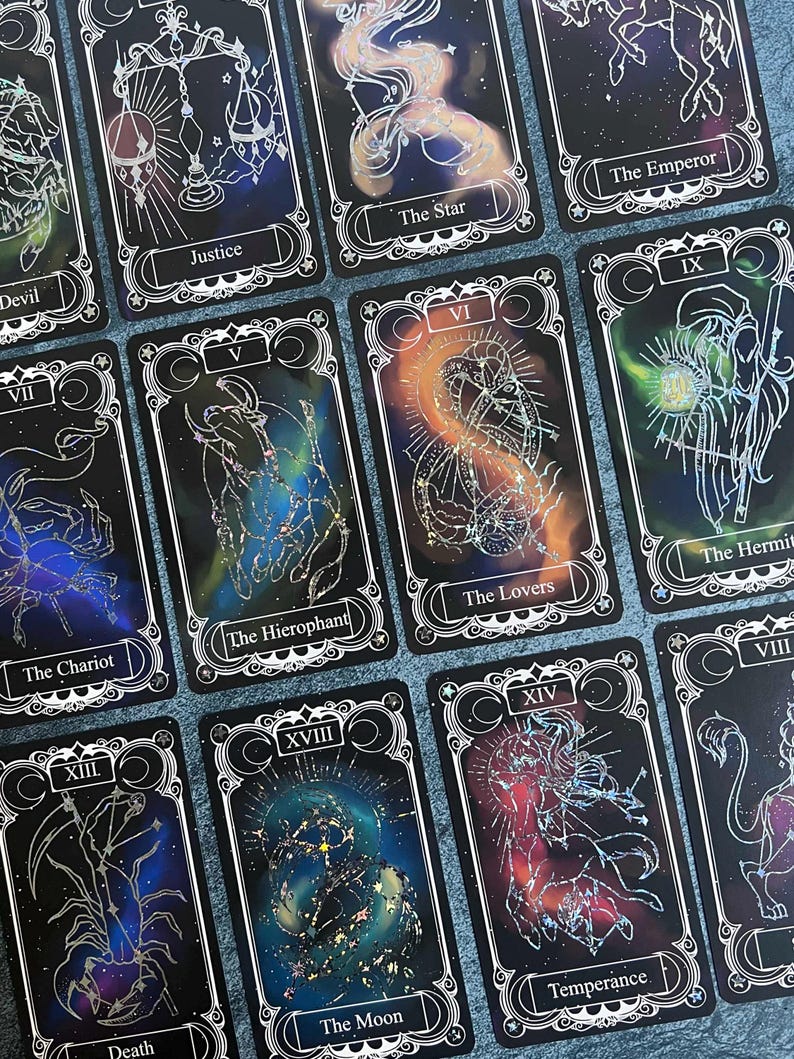 May include: A collection of rectangular tarot cards featuring black backgrounds with colorful nebula-like patterns and white line art illustrations. Each card displays a Roman numeral, a title such as Justice, The Star, The Emperor, The Hierophant, The Lovers, The Hermit, The Chariot, Death, The Moon, and Temperance.