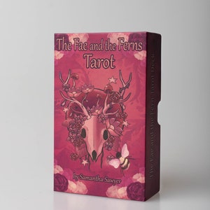 May include: A pink box with a skull and floral design. The box is for a tarot deck called "The Fae and the Ferns Tarot" by Samantha Sawyer.