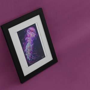 May include: Framed art print featuring a vibrant illustration of a jellyfish. The artwork showcases a jellyfish with a pink bell, flowing tentacles, and a mix of purple, green, and blue hues against a dark background. The print is set in a black frame with a white mat.