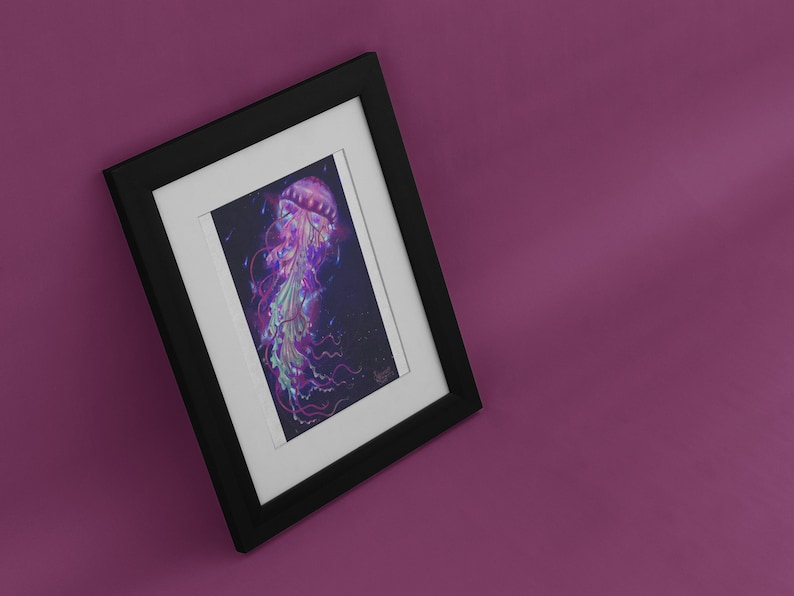 May include: Framed art print featuring a vibrant illustration of a jellyfish. The artwork showcases a jellyfish with a pink bell, flowing tentacles, and a mix of purple, green, and blue hues against a dark background. The print is set in a black frame with a white mat.