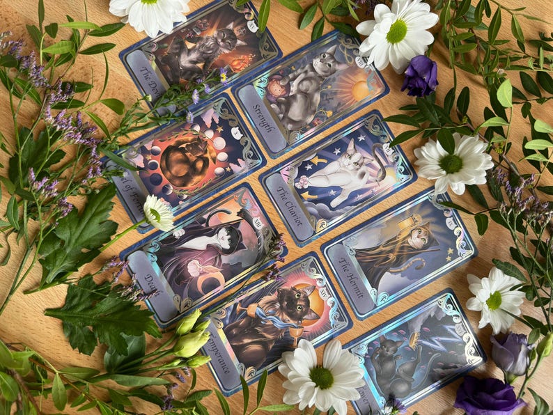 May include: A collection of eight rectangular tarot cards featuring cat illustrations, each with a blue border and text labels including The Devil, Strength, Wheel of Fortune, The Chariot, Death, The Hermit, Temperance, and a final unlabeled card.