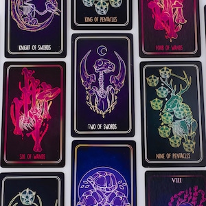 May include: A collection of tarot cards with dark backgrounds and gold and neon illustrations. The cards feature images of skeletons, mushrooms, and other mystical symbols. Text on the cards includes "Knight of Swords", "King of Pentacles", and "Two of Swords".