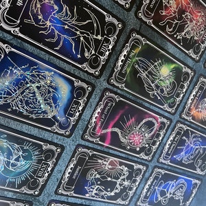 May include: A collection of tarot cards featuring black backgrounds with colorful nebula-like designs and white line art illustrations. Each card displays a unique title such as Death, Temperance, The Hermit, Wheel of Fortune, Justice, and The Hanged Man.