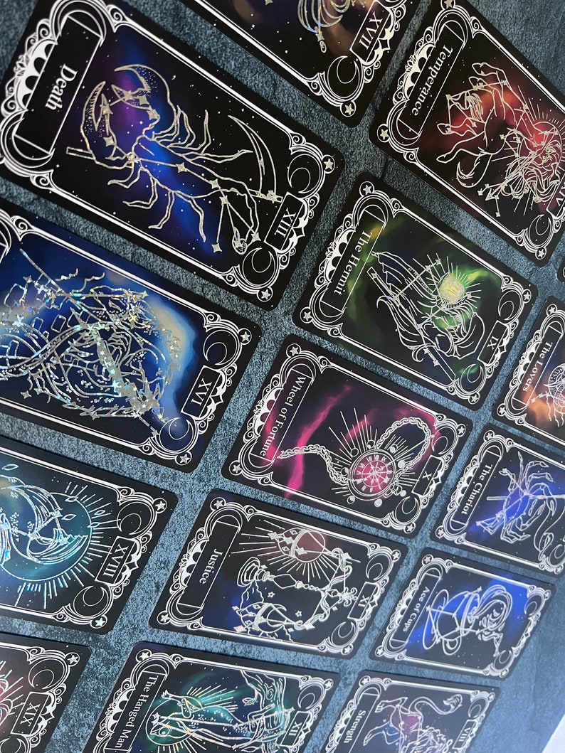 May include: A collection of tarot cards featuring black backgrounds with colorful nebula-like designs and white line art illustrations. Each card displays a unique title such as Death, Temperance, The Hermit, Wheel of Fortune, Justice, and The Hanged Man.