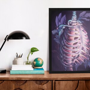 May include: A framed print of a skeletal ribcage with purple and pink flowers growing through it. The background is a dark purple.