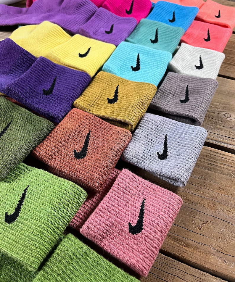 Pode incluir: Uma pilha de meias coloridas com um logotipo Nike swoosh. As meias est&atilde;o dispostas em um padr&atilde;o de arco-&iacute;ris, com cada meia de uma cor diferente.