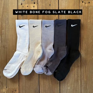 Pode incluir: Cinco pares de meias de cano alto em diferentes cores: branco, osso, nevoeiro, ard&oacute;sia e preto. Cada meia tem um logotipo Nike Swoosh preto.