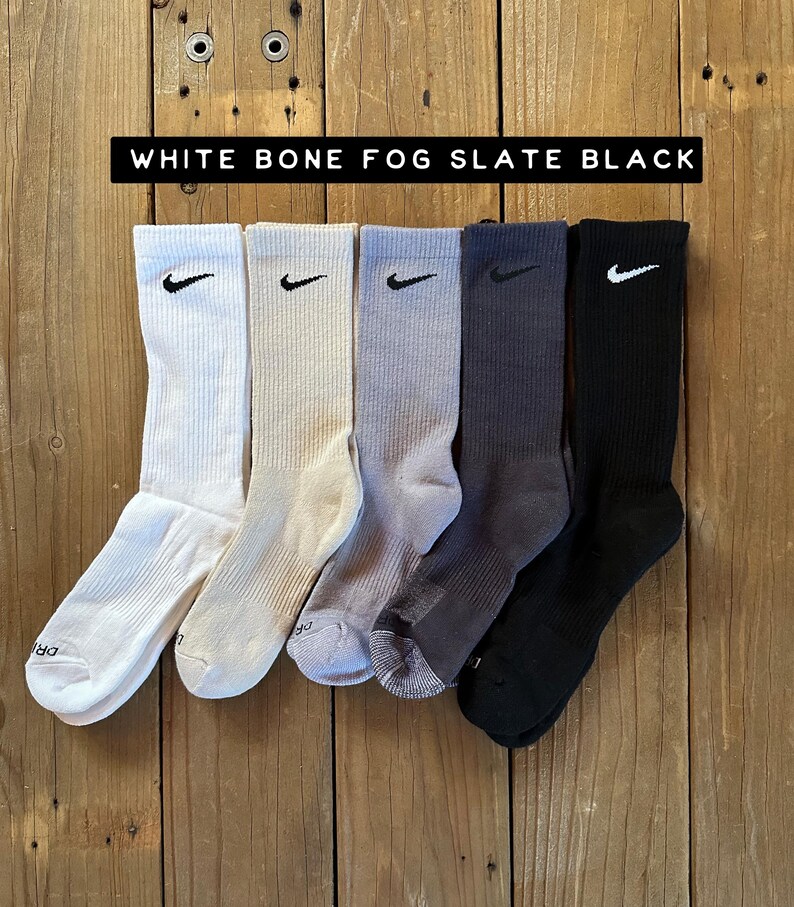 Pode incluir: Cinco pares de meias de cano alto em diferentes cores: branco, osso, nevoeiro, ard&oacute;sia e preto. Cada meia tem um logotipo Nike Swoosh preto.