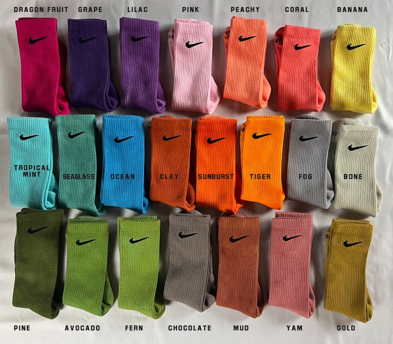 Pode incluir: Um conjunto de 24 meias coloridas com um logotipo da Nike. As meias est&atilde;o dispostas em quatro filas de seis meias cada. As meias s&atilde;o etiquetadas com nomes como "Fruta do Drag&atilde;o", "Uva", "Lil&aacute;s", "Rosa", "P&ecirc;ssego", "Coral", "Banana", "Menta Tropical", "Algas Marinhas", "Oceano", "Argila", "Explos&atilde;o de Sol", "Tigre", "N&eacute;voa", "Osso", "Pinho", "Abacate", "Samambaia", "Chocolate", "Lama", "Inhame" e "Ouro".