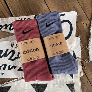Pode incluir: Dois pares de meias de algod&atilde;o tingidas &agrave; m&atilde;o, um par de cor castanho cacau e o outro de cor azul ard&oacute;sia. Ambos os pares t&ecirc;m um logotipo branco Nike em forma de swoosh no lado. A embalagem diz "1 par - grande" e "meias de algod&atilde;o tingidas &agrave; m&atilde;o".