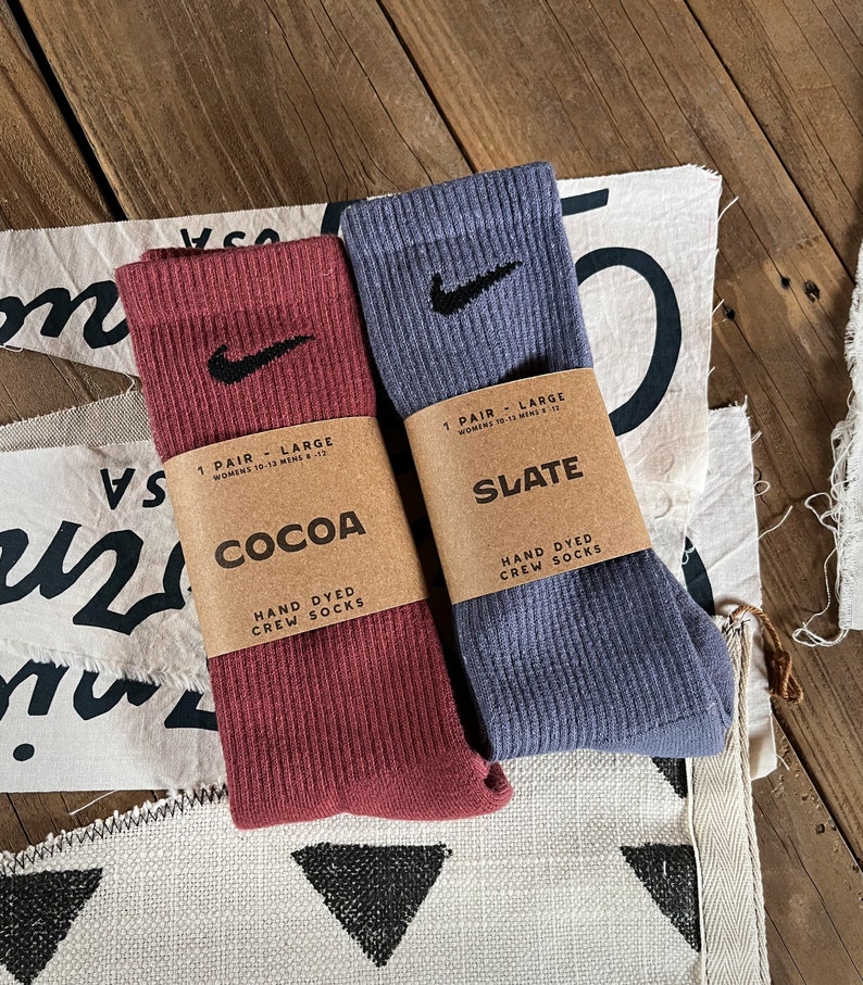 Pode incluir: Dois pares de meias de algod&atilde;o tingidas &agrave; m&atilde;o, um par de cor castanho cacau e o outro de cor azul ard&oacute;sia. Ambos os pares t&ecirc;m um logotipo branco Nike em forma de swoosh no lado. A embalagem diz "1 par - grande" e "meias de algod&atilde;o tingidas &agrave; m&atilde;o".