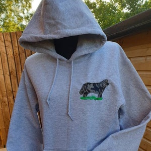 May include: A gray hooded sweatshirt with a black and white embroidered dog on the front. The dog is standing on a green patch of grass.