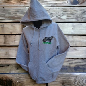 May include: A gray hooded sweatshirt with a black and white embroidered dog on the front. The dog is standing on a green patch of grass.