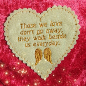 May include: A beige felt heart with gold embroidery that reads "Those we love don't go away, they walk beside us everyday."  Two gold angel wings are embroidered below the text.