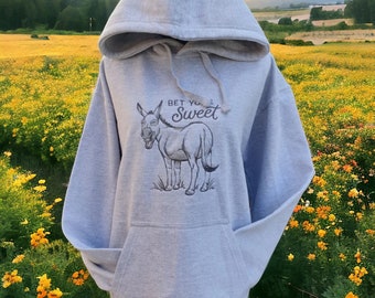 Puede incluir: Una sudadera con capucha gris con una ilustración en blanco y negro de un burro con el texto "Bet you're sweet" en la parte delantera.