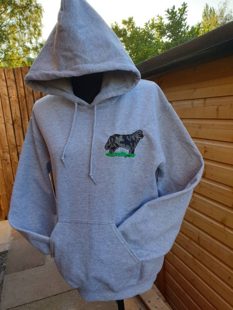 May include: A gray hooded sweatshirt with a black and white embroidered dog on the front. The dog is standing on a green patch of grass.