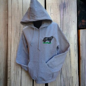 May include: A gray hooded sweatshirt with a black and white dog embroidered on the front. The dog is standing on a green patch of grass.