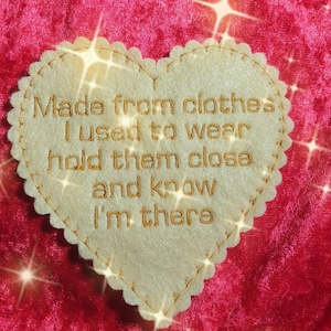 Könnte beinhalten: Ein herzförmiger Filz-Patch mit goldener Stickerei, auf dem steht: "Hergestellt aus Kleidung, die ich trug, halte sie nah und wisse, dass ich da bin".