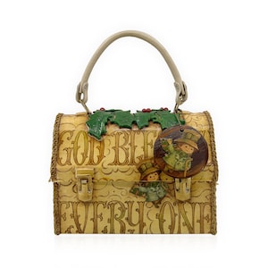 May include: A vintage-style handbag with a light tan background and the words "GOD BLESS EVERYONE" printed on the front. The bag features a beige handle, a decorative holly and berry accent, and a wooden tag with a cartoon illustration.