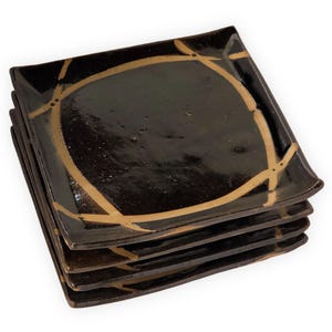 May include: A stack of four black square ceramic plates with a gold geometric design. The plates are stacked on top of each other.