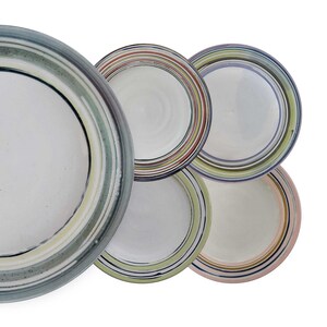 May include: Set of five ceramic plates with colorful, striped designs. The plates are white with various colored stripes, including green, blue, pink, and yellow.