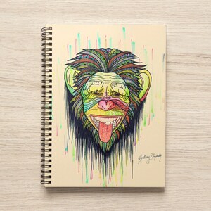 May include: A spiral bound notebook with a colorful illustration of a monkey's face. The monkey has a green, yellow, and red face with a black and white patterned design. The background is a light beige with colorful vertical lines.