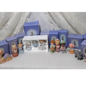 May include: A set of 12 porcelain figurines depicting the Nativity scene, including Mary, Joseph, baby Jesus, the three wise men, a shepherd, an angel, a camel, a donkey, a sheep, and a star. The figurines are packaged in individual boxes with the words "Heavenly Blessings" printed on them.