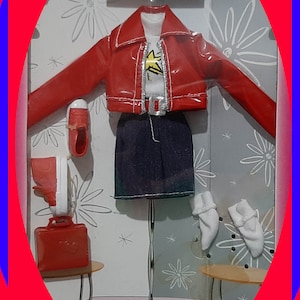 May include: A Teen Skipper doll clothing set in original packaging featuring a red cropped jacket, a white t-shirt with a yellow star graphic, a dark blue skirt, red sneakers, a red handbag, and white socks. The set is displayed on a stand.