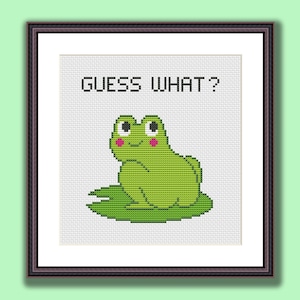 May include: Cross stitch pattern featuring a green frog with pink cheeks sitting on a lily pad. The text "GUESS WHAT?" is above the frog.