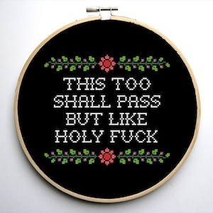 May include: Black embroidery hoop with white text that reads "This too shall pass but like holy fuck" with green and pink floral accents.