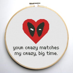 Puede incluir: Un aro de bordado blanco con un corazón rojo con un diseño de máscara negra de Deadpool. El texto "your crazy matches my crazy, big time." está debajo del corazón.