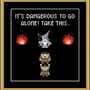 May include: Cross-stitch art framed in gold. The black background features pixelated images of a wizard, two flames, and two figures. The text reads, "IT'S DANGEROUS TO GO ALONE! TAKE THIS."