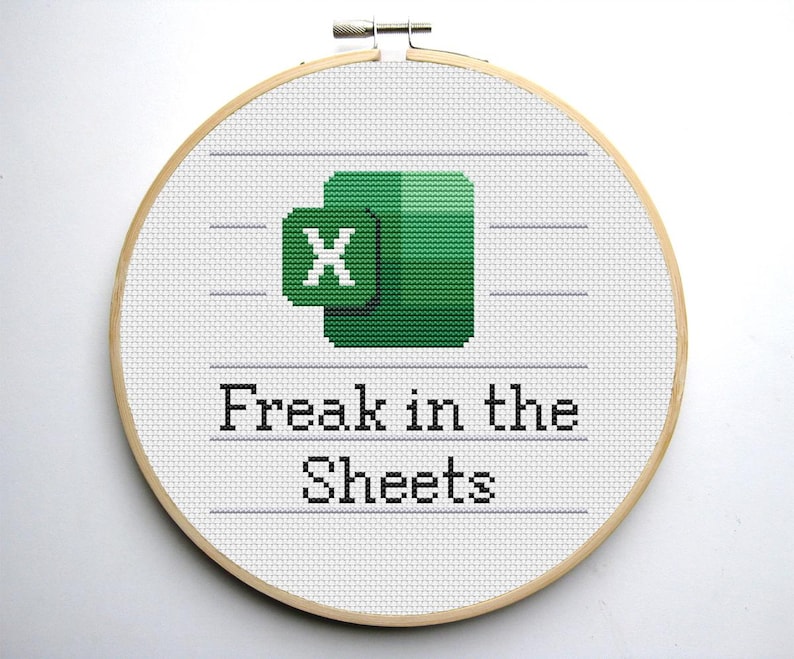 Puede incluir: Un bastidor de bordado con punto de cruz que presenta el logotipo de Microsoft Excel en verde y blanco, con el texto "Freak in the Sheets" bordado debajo. El bordado est&aacute; en un bastidor redondo de madera.
