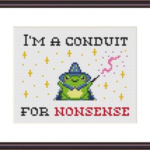 Puede incluir: Arte de punto de cruz en un marco marrón. El diseño presenta una rana verde con sombrero y capa de mago, sosteniendo una varita. El texto dice "I'M A CONDUIT FOR NONSENSE" con acentos de estrellas y magia.