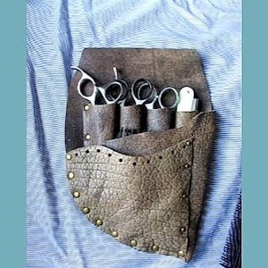 Peut inclure: Une ceinture à outils en cuir marron avec plusieurs poches pour ranger des ciseaux et des peignes. La ceinture est décorée de clous métalliques et a une surface texturée.
