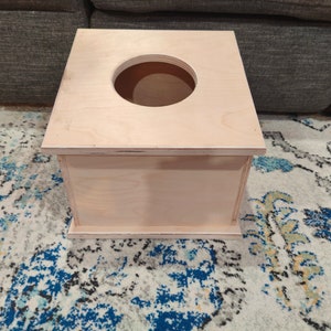 May include: A plain wooden box with a round opening in the top. The box is made of light wood and has a natural finish.