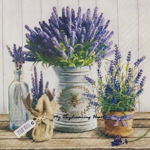 May include: A still life featuring lavender flowers in a blue and white pitcher, a glass bottle, and a brown pot with a white and blue ribbon. The pitcher has the word "Lavande" and a bee design. The text "My Daydreaming Heart" is visible on the table.