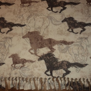 Könnte beinhalten: Beige Fleece-Decke mit einem sich wiederholenden Muster von galoppierenden Pferden in Braun- und Schwarztönen. Die Decke hat einen Fransenrand. Das Design umfasst sowohl vollflächige als auch umrissene Pferdeillustrationen.