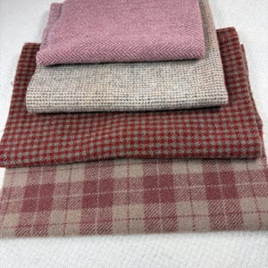 May include: A stack of four folded fabric swatches. The top piece is pink with a herringbone pattern. Below it is a beige and gray speckled fabric. The third is a red and gray houndstooth pattern, and the bottom piece is a pink and beige plaid.