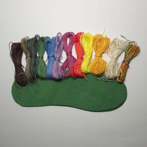 May include: A set of 10 spools of waxed thread in various colors, including brown, green, blue, purple, red, yellow, orange, white, and green. The spools are arranged in a rainbow pattern on a green leather surface.